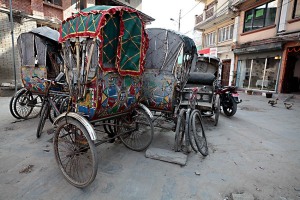 L'evoluzione dei risciò, carrelli a due ruote: anticamente erano condotti da uomini che li trainavano a piedi nudi, poi si sono trasformati in "ciclorisciò", il conducente pedalava una bicicletta attaccata al carrello, infine si sono trasformati in autorisciò, i carrelli in quest'ultimo caso vengono motorizzati. Dintorni di Durbar Square, Kathmandu, Nepal 2018
