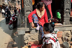Tra le colonne di legno finemente cesellate dei portici di Durbar Square a Patan, le donne nepalesi di etnia Newari espongono corone di fiori, monili realizzati artigianalmente e arachidi, Nepal 2018