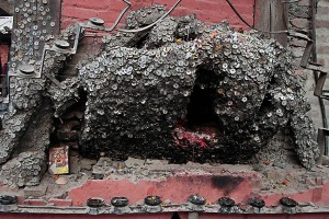 A nord di Durbar Square, nella città vecchia di Kathmandu e precisamente nella piazza di "Bangemudha" (che significa legno contorto) ci si imbatte in questo ceppo di legno irregolare sul quale sono state inchiodate migliaia di monete: sono offerte al Dio del mal di denti che viene riprodotto attraverso una piccola statuetta inserita nell'incavo di questo rudimentale tronco, Nepal 2018