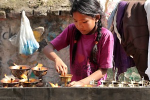 Nei pressi dello Stupa di Bodhnath una bambina nepalese è intenta a pulire i candelabri in ottone che verranno offerti dai devoti durante la "puja" (preghiera devozionale) alle diverse Divinità, Nepal 2018