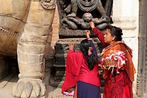Due fedeli Hindu adorano attraverso la pratica della Puja (la preghiera rituale) la Divinità rappresentata dalla statua intagliata in pietra ("Murti"), pregando, facendo offerte ("Upachara") di fiori, riso e frutta, Patan, Nepal 2018