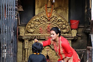 Allontanandosi dalla affollata e caotica Durbar Square di Kathmandu, si può percorrere la Maru Tole ("Tole" significa strada) per giungere davanti a questo minuscolo tempio dorato dedicato al Dio Ganesh, tra i quattro più importanti di tutta la Valle: una mamma, dopo la tradizionale "puja" (preghiera rituale con donazione di offerte alla Divinità: nel caso di offerte di alimenti gli stessi verranno poi consumati dall'offerente in quanto dopo il rito divengono "Prasada", cioè cibo benedetto e purificato), segna sulla fronte della sua bambina il "Tilaka" o "Pundra", un segno rosso che si crede abbia una funzione curativa e protettiva. La miscela utilizzata per disegnarlo è rinfrescante e viene applicata sul punto di concentrazione delle energie spirituali al centro della fronte, tra le sopracciglia (tale punto prende il nome di "Ajna Chakra"). Si crede che il Tilaka procuri conforto spirituale e protezione dagli spiriti maligni, dalla sfortuna e dalle forze del male. Nepal 2018