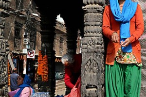 Nello splendido porticato che circonda Durbar Square a Patan, sorretto dalle antiche colonne in legno finemente intarsiato dai mastri scalpellini nepalesi, alcune donne preparano le corone di fiori dalle vivaci tonalità, Nepal 2018