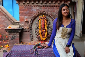 Seduta accanto al piccolo tempio dedicato al Dio Ganesh (il Dio Elefante) questa giovane ragazza nepalese è una venditrice ambulante che propone collane e braccialetti tradizionali ai suoi potenziali clienti, il suo nome è Urmila Bohora. Dintorni di Durbar Square, Patan, Nepal 2018