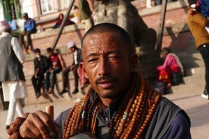 Un venditore ambulante di collane e bracciali tradizionali, nel centro della piazza principale di Patan, fa suonare la campana tibetana per attrarre possibili clienti (è un antico strumento musicale originario del Tibet: produce un suono puro ed una vibrazione armonica, spesso utilizzata come strumento vibrazionale. La sua origine risale a circa 3.000 anni fa in una fase storica antecedente alla nascita del Buddhismo. In quel lontano periodo, secondo la leggenda, si praticava un rituale che conferiva al gong, alle campane ed ai cimbali la capacità di guarire il corpo, oltre ad avvicinare l'uomo alla Divinità. Attualmente è apprezzato anche come strumento terapeutico). Nepal 2018.