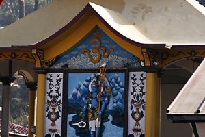 L'immagine dell'esterno del Tempio Hindu di Pashupatinath: l'immagine del Dio Shiva risalta sulla facciata insieme al simbolo dell'Om (attraverso la meditazione dell'Om, simbolicamente posto al centro del cuore, secondo la religione Hindu, si perviene alla realizzazione conoscitiva dell'assoluto. Om cinge passato, presente, futuro e tutto ciò che esiste oltre queste tre fasi temporali. Rappresenta la triplice sapienza, i tre Veda fondamentali, "Rigveda", "Samaveda", "Yajurveda", l'alfa e l'omega del ciclo cosmico, i cui tre momenti costitutivi sono rappresentati dalla Trimurti, cioè i tre aspetti della divinità suprema, che si manifesta nelle tre divinità di Brahma, il creatore, Vishnu, il preservatore, Siva, il distruttore. Viene considerato il suono primordiale che ha dato origine alla creazione, che viene interpretata come la manifestazione stessa di questo suono. Secondo le tradizioni hiunduiste, il mantra Om rappresenta la sintesi e l'essenza di ogni mantra, preghiera, rituale, testo sacro, essere celeste o aspetto divino. Proprio per questo la sillaba Om viene recitata in apertura delle letture religiose, delle pratiche relative alle "Puja" e delle "Yajna", cioè durante le offerte o invocazioni). Nepal 2018.