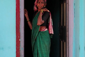 L'ingresso di una abitazione nel villaggio di Belur: la padrona di casa sull'uscio, tra i colori pastello delle pareti e delle cornici della porta, sembra completare l'armonia di questa istantanea. Regione del Karnataka, India 2015.